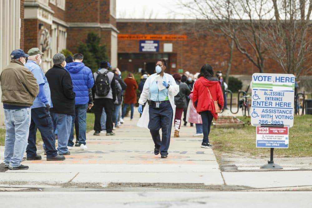A woman hands out surgical masks to people standing in line to vote in Wisconsin’s spring primary election on April 7, 2020 at Riverside High School in Milwaukee, WI. (Sara Stathas for the Washington Post via Getty Images)