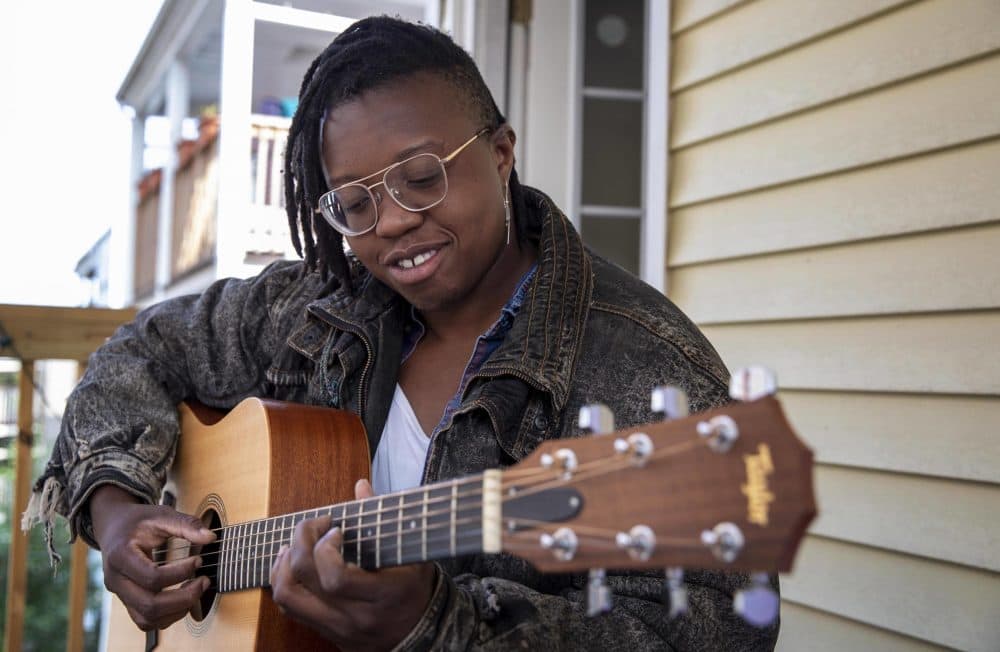 Singer and songwriter Anjimile plays guitar on a porch in Jamaica Plain, Boston. (Robin Lubbock/WBUR)