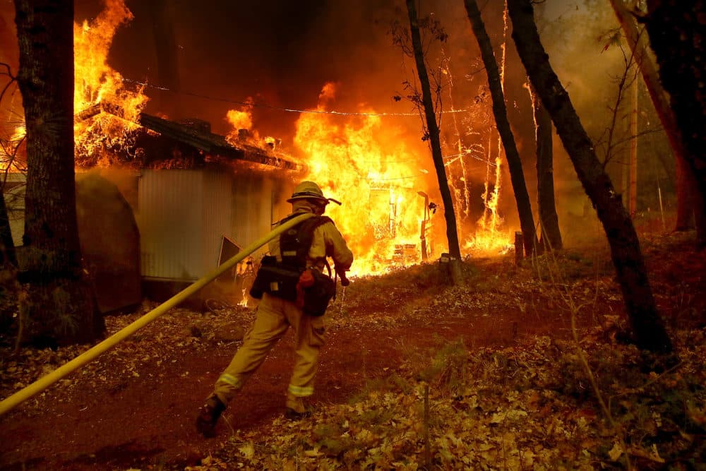 A Cal Fire firefighter pulls a hose towards a burning home as the Camp Fire moves through the area on Nov. 9, 2018 in Magalia, California. (Justin Sullivan/Getty Images)