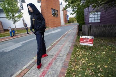 Vistiors to Salem stop and watch a man on stilts and wearing a Halloween costume walk past them on Charter Street. Signs are posted around Downtown Salem reminding everyone it is mandatory to wear a mask in public to help prevent the spread of the coronavirus.(Jesse Costa/WBUR)