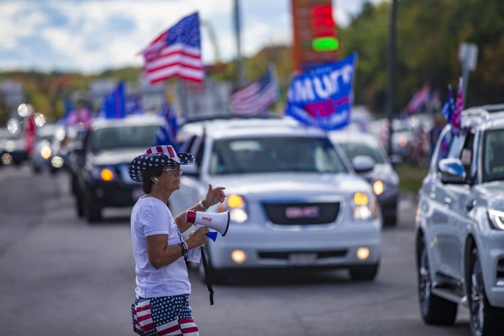 Lorraine Cambria waves cars to leave the Lexington Service Center on Route 95, as they merge with the rest of the caravan to drive to the rally in Londonderry, N. H. (Jesse Costa/WBUR)