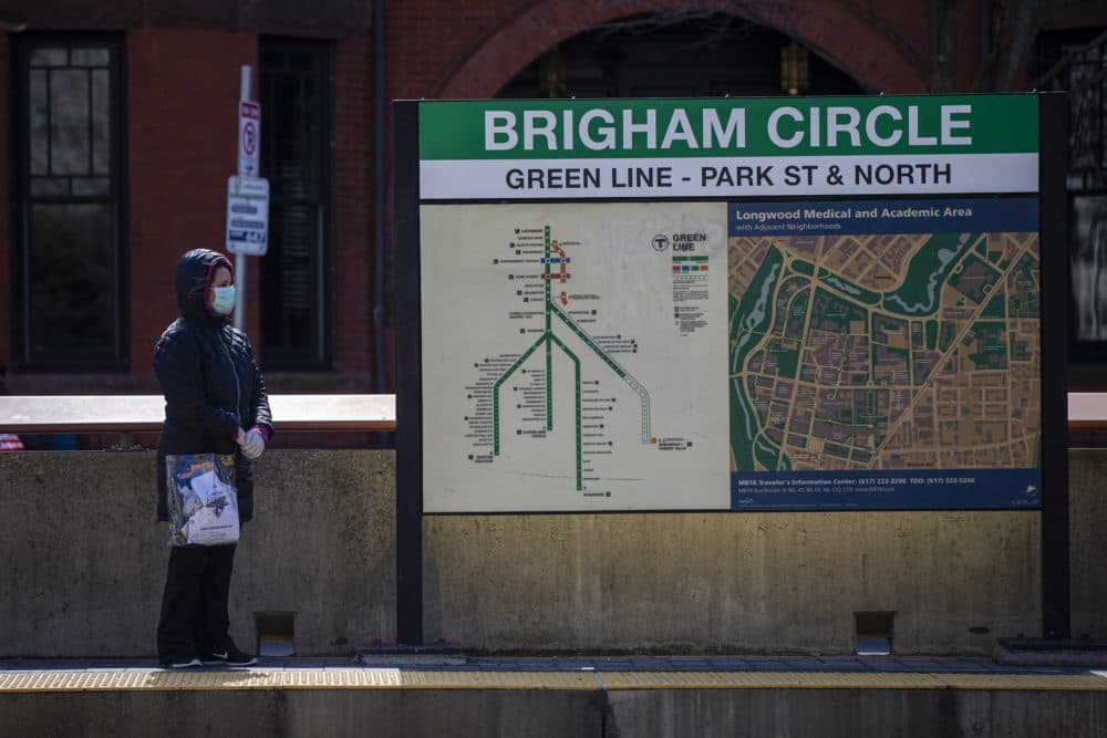 A woman wearing a mask waits for an MBTA Green Line train at Brigham Circle Station. (Jesse Costa/WBUR)