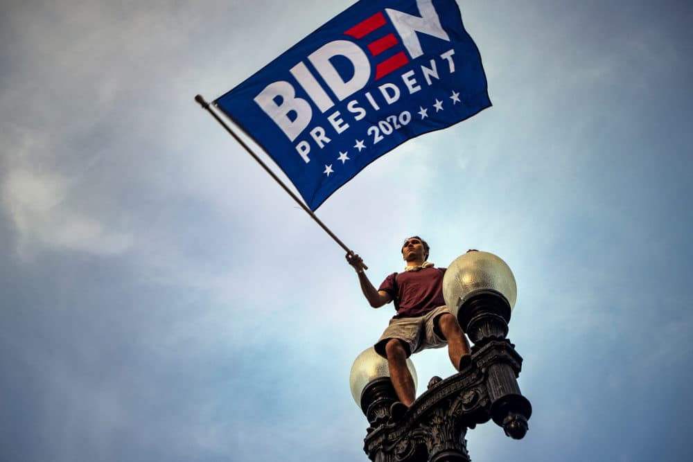 Tristan Homewood waves a Biden campaign flag as he stands on a street lamp on the corner of Boylston and Charles Streets to celebrate Joe Biden’s presidential victory. (Jesse Costa/WBUR)