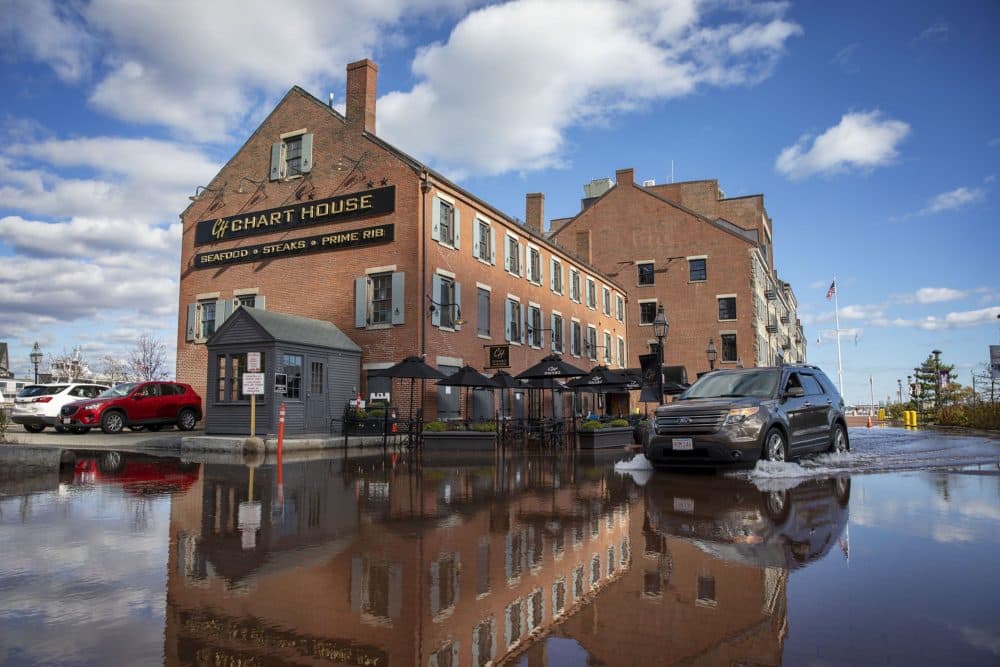A car drives through flood water by the Chart House on Boston's Long Wharf during a November king tide. (Robin Lubbock/WBUR)