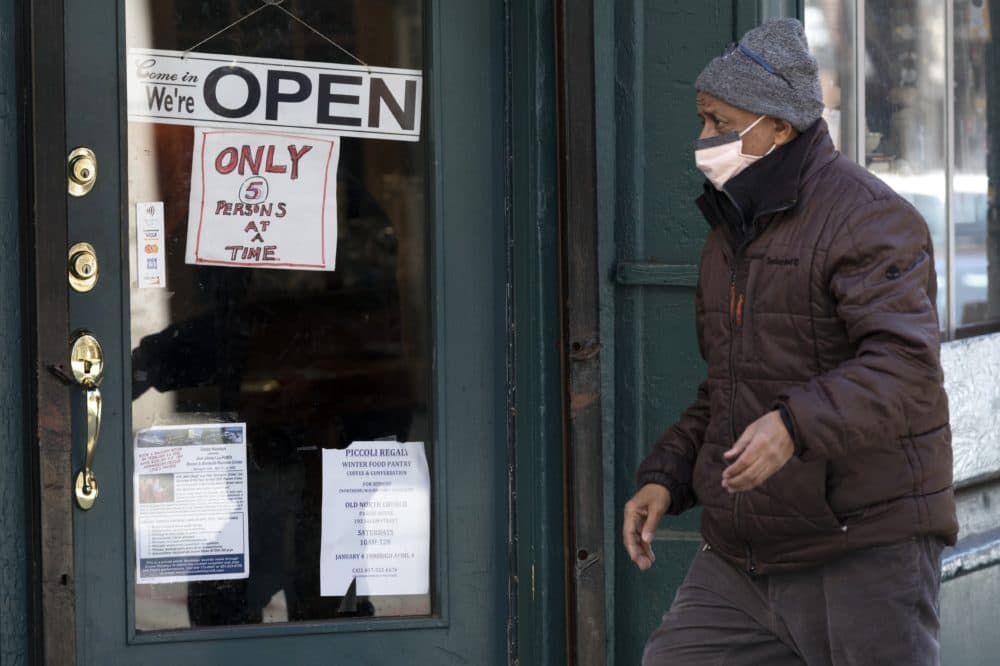 A man walks past a shop, open for business in the North End neighborhood of Boston, but only allowing five customers at a time, March 21, 2020. (Michael Dwyer/AP)