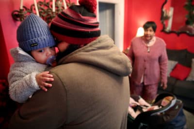 David Nelligan picks up his son, while Dorothy Williams looks on at Dottie's Family Childcare in Dorchester in March 2020. Dorothy normally cares for 10 children but was down to two that day as parents increasingly worked from home and removed their children from situations in which they could contract coronavirus. (Craig F. Walker/The Boston Globe via Getty Images)