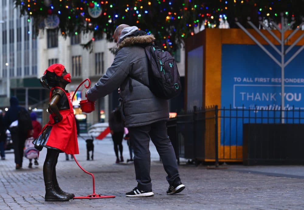 A man puts a donation into the red kettle next to the 'Fearless Girl' statue dressed in a Salvation Army uniform in front the of New York Stock Exchange on Dec. 10, 2020. The traditional Red Kettle donations started in Sept. 2020, some two months earlier than usual. The Salvation Army said the earlier start was due to the COVID-19 pandemic. (Angela Weiss/AFP/Getty Images)