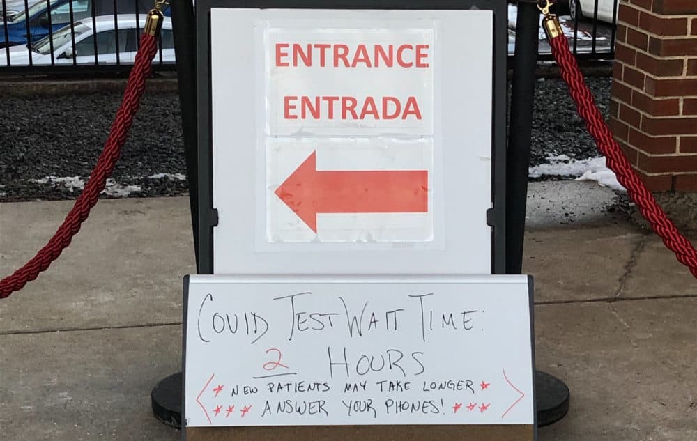 A sign posted outside the Family Health Center of Worcester, indicating the long wait time for COVID tests. (Deborah Becker/WBUR)