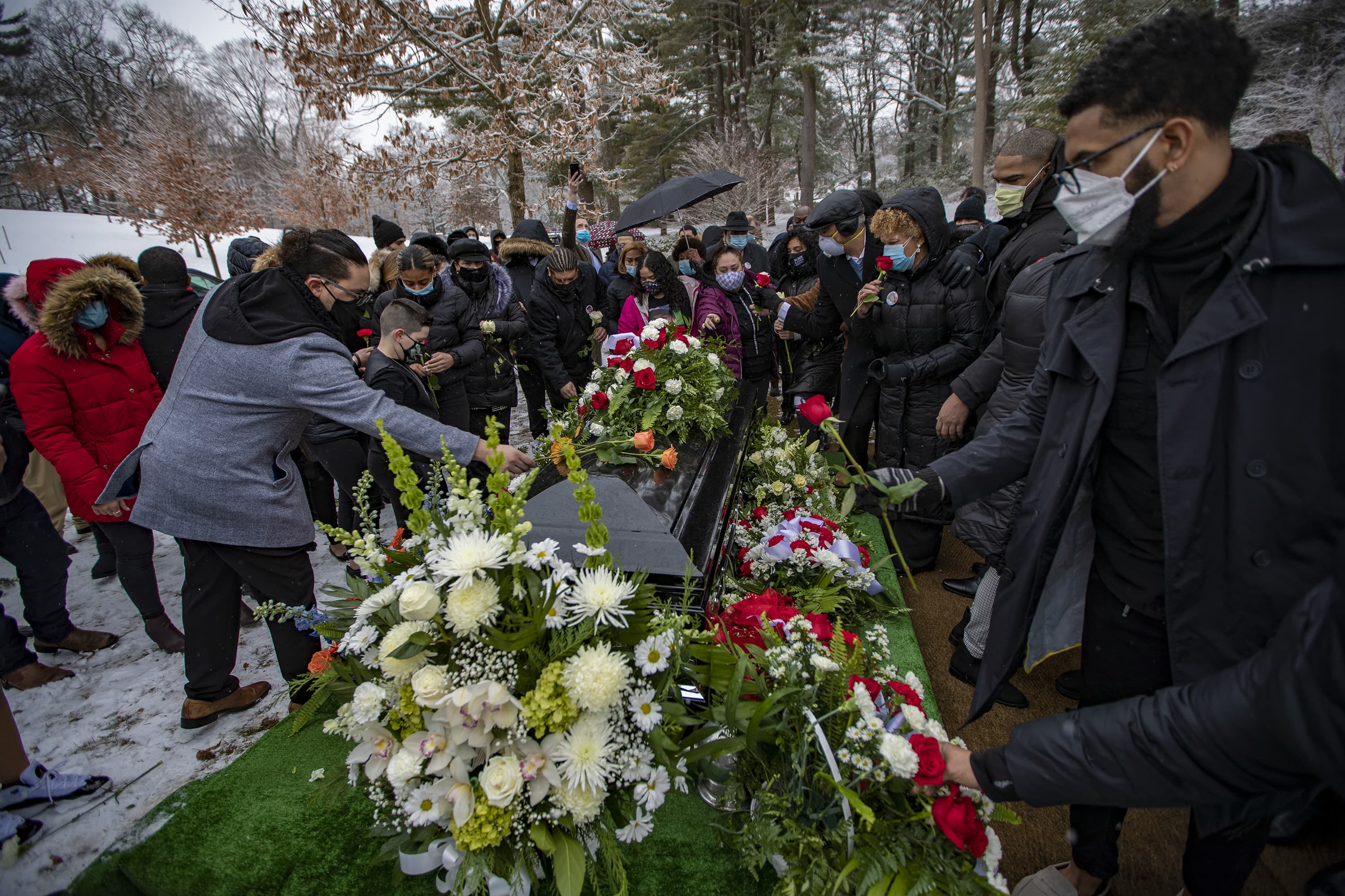 Friends and family place flowers on top of Henry Tapia's casket at Forest Hills Cemetery. (Jesse Costa/WBUR)