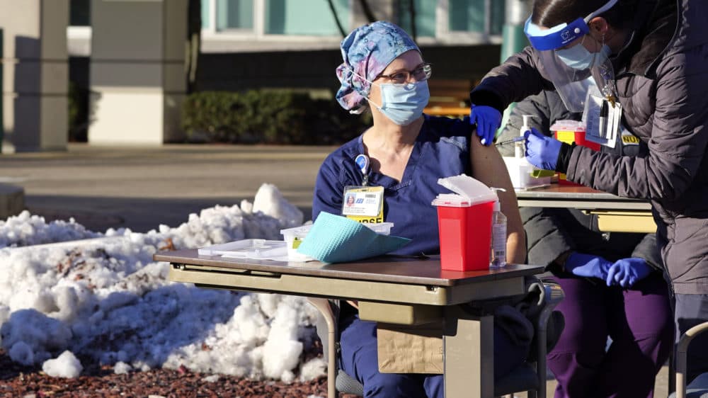 With temperatures slightly below freezing, intensive care unit nurse Heidi Kukla, center, sits next to a snow bank as she is injected with the Pfizer-BioNTech COVID-19 vaccine outside the Elliot Hospital, Dec. 15, 2020, in Manchester, N.H. (Charles Krupa/AP)