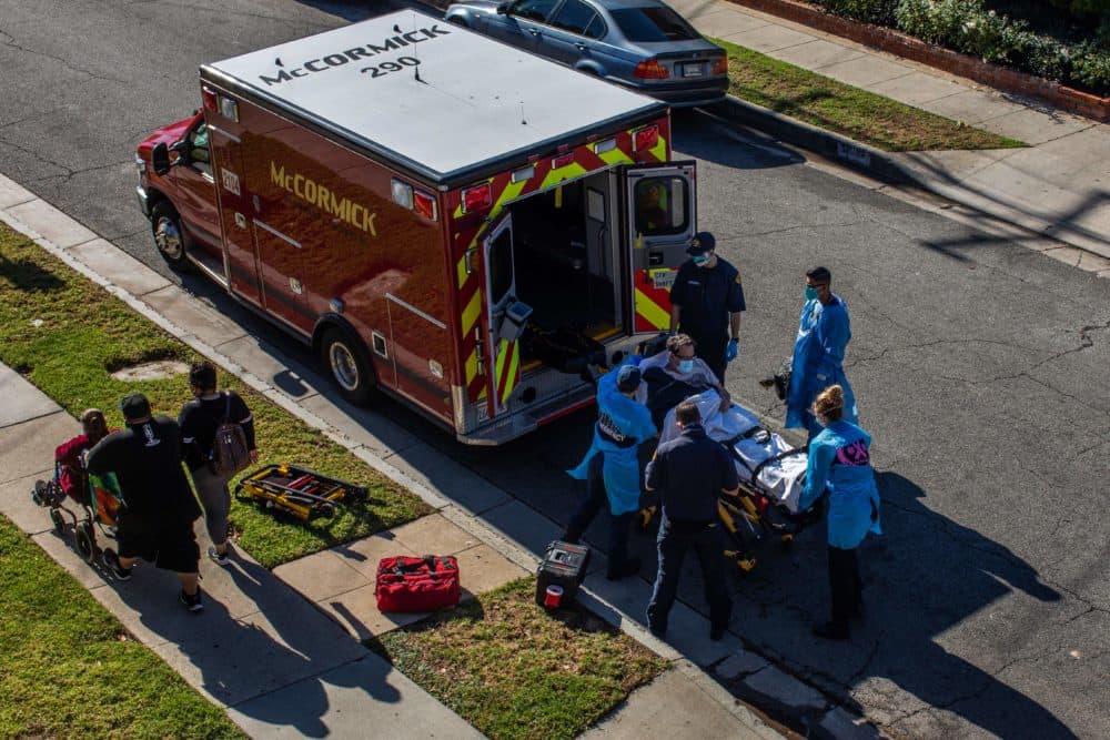 After administering him with oxygen, County of Los Angeles paramedics load a potential COVID-19 patient in the ambulance before transporting him to a hospital in Hawthorne, California on Dec. 29, 2020 as a family walks by. (Apu Gomes/AFP via Getty Images)
