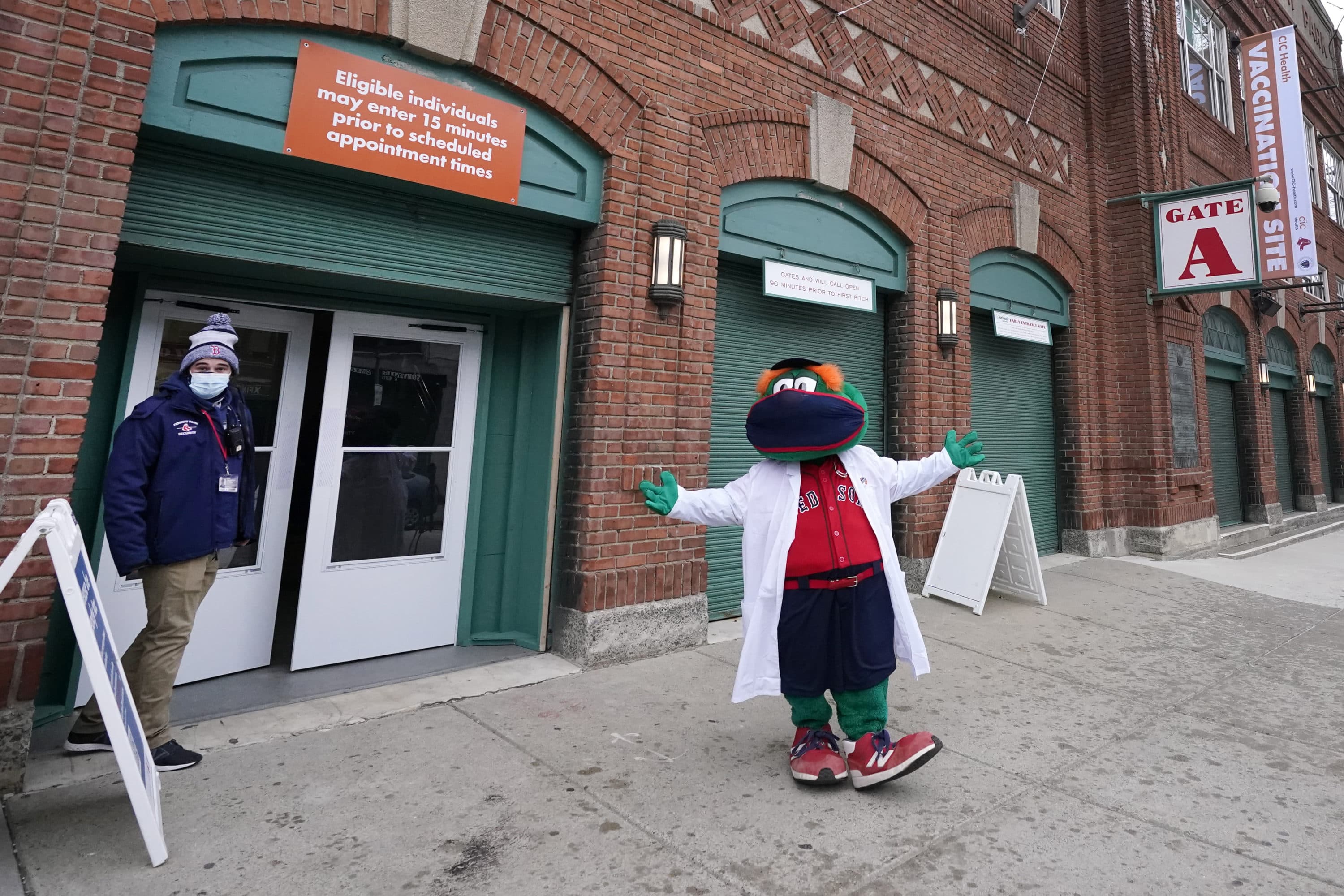 Boston Red Sox mascot, Wally the Green Monster, gestures while dressed in a medical white coat outside Fenway Park, Monday Feb. 1, 2021, in Boston. Fenway Park is one of several large COVID-19 vaccination sites in the Boston area. (Elise Amendola/AP)