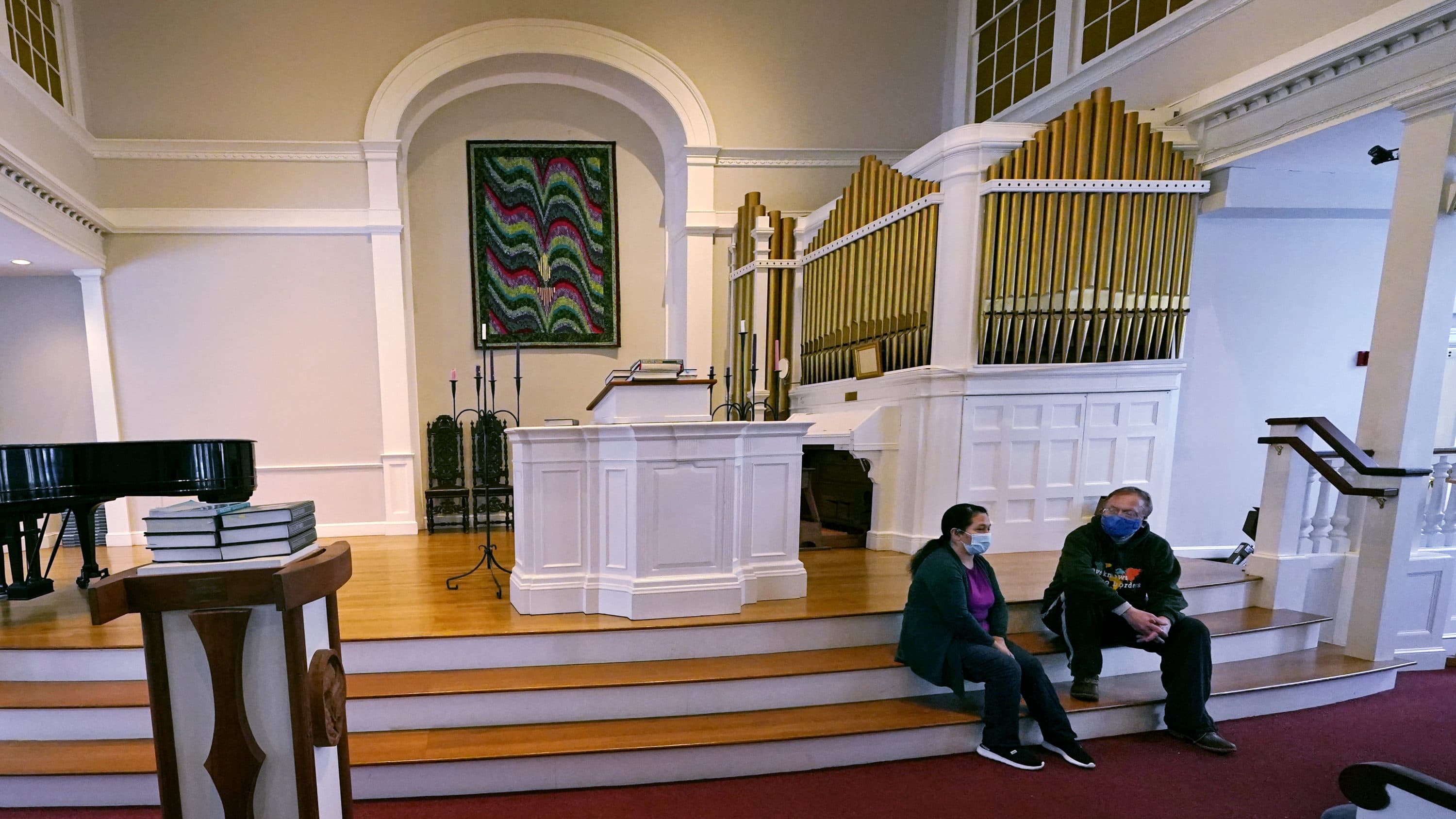 Maria Macario, left, talks with Rev. John Gibbons while seated on the steps to the altar at the First Parish church in Bedford. (Charles Krupa/AP)