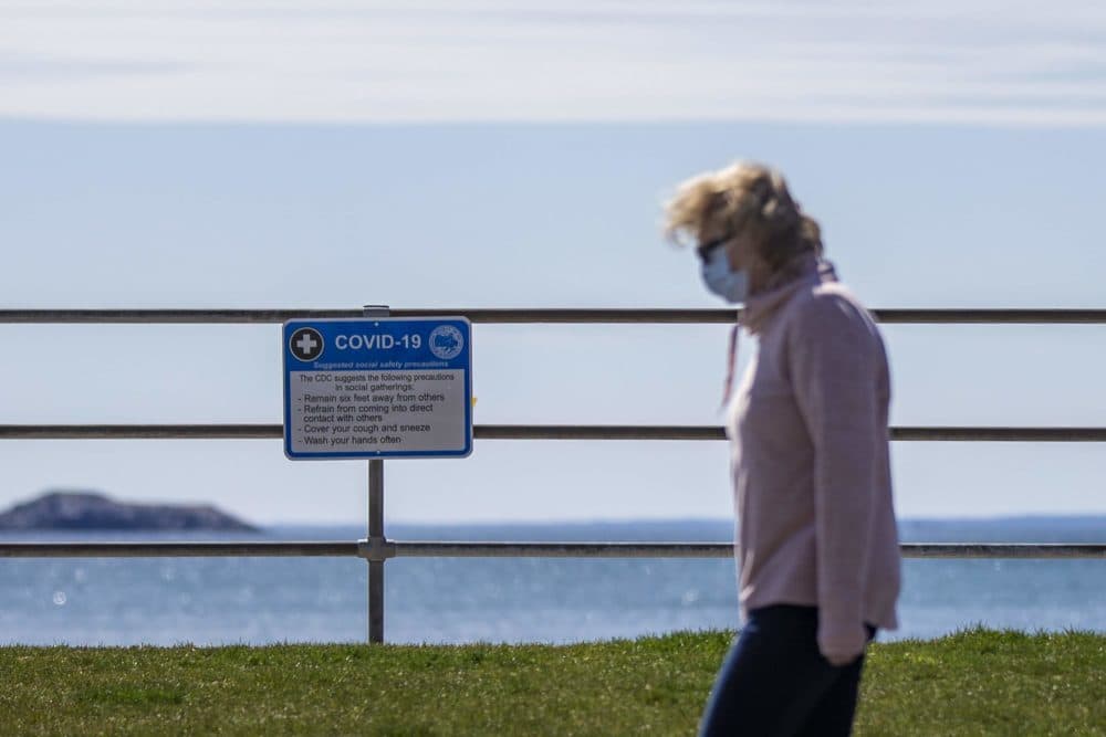 A woman walks past a sign at King's Beach in Swampscott listing the CDC recommendations for social gathering during the pandemic in April 2020. (Jesse Costa/WBUR)