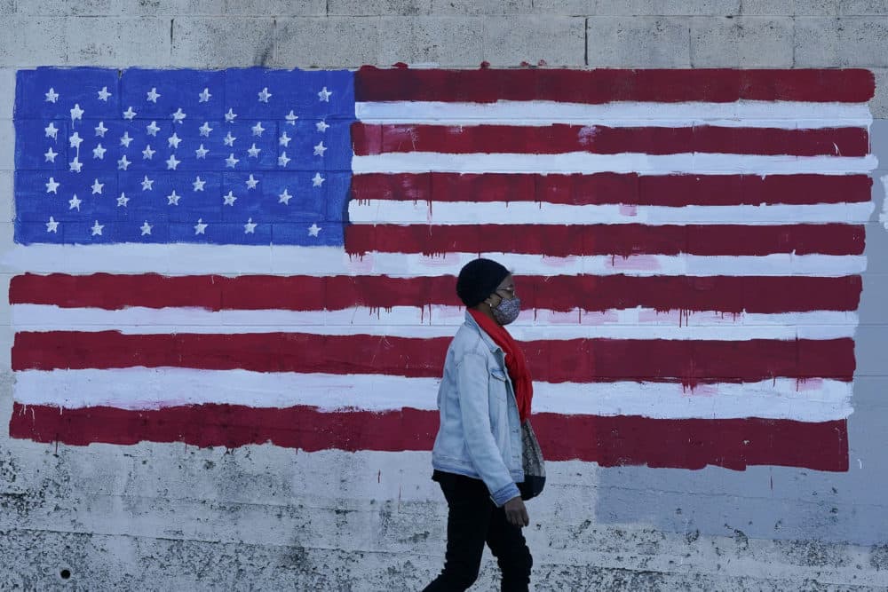 A woman wears a mask while walking past an American flag painted on a wall. (Jeff Chiu/AP)