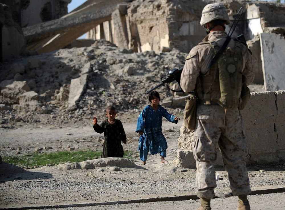 Afghan children watch as a US Marine from 2nd Battalion, 1st Marines Regiment stands in front of ruins in Garmser, Helmand Province, on March 13, 2011. (Adek Berry/AFP via Getty Images)