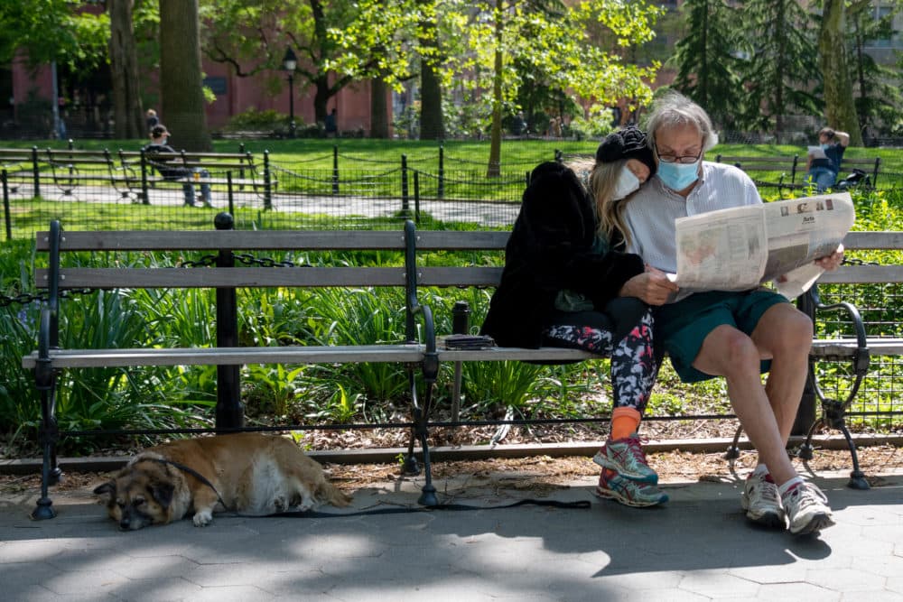 A couple wearing masks sits together reading the newspaper in New York City. (Alexi Rosenfeld/Getty Images)