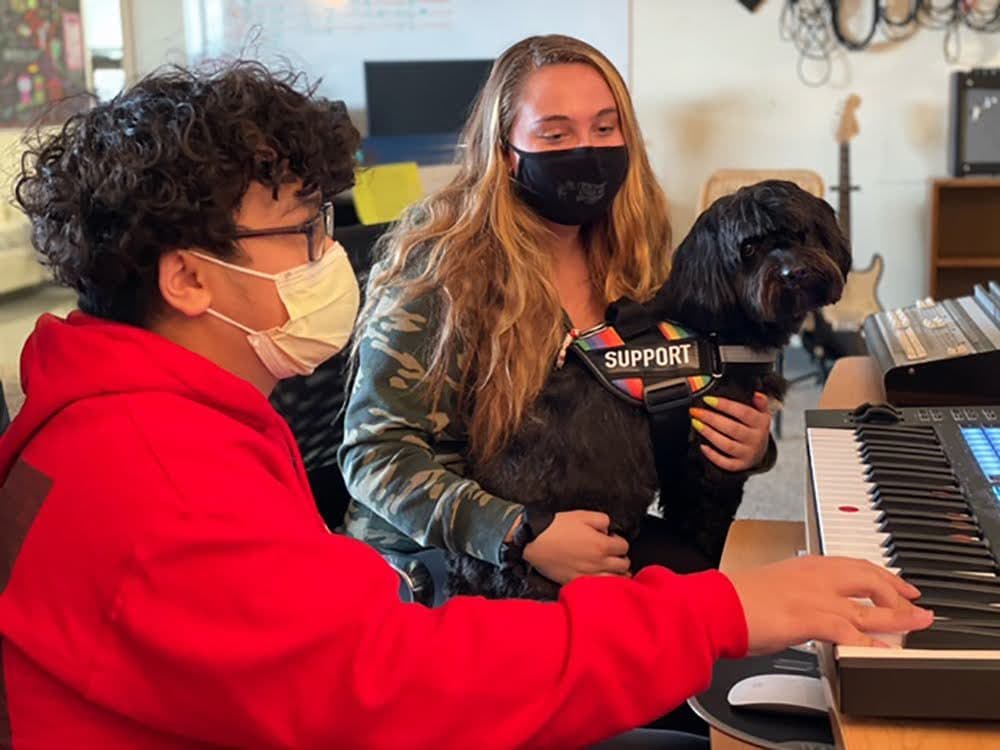 Stephen Phan and Carly Baker sit by the piano with service dog, Franklin, at North Shore Recovery High in Beverly. (Courtesy Mary Devin/North Shore Recovery High School)