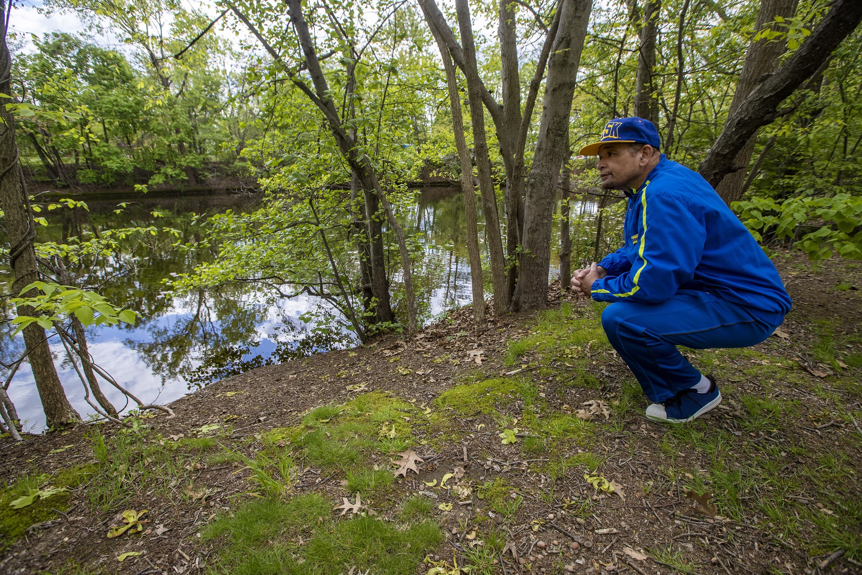 Poet Terry Carter kneels down to gaze at the Mystic River, along the banks in West Medford where he grew up. (Jesse Costa/WBUR)