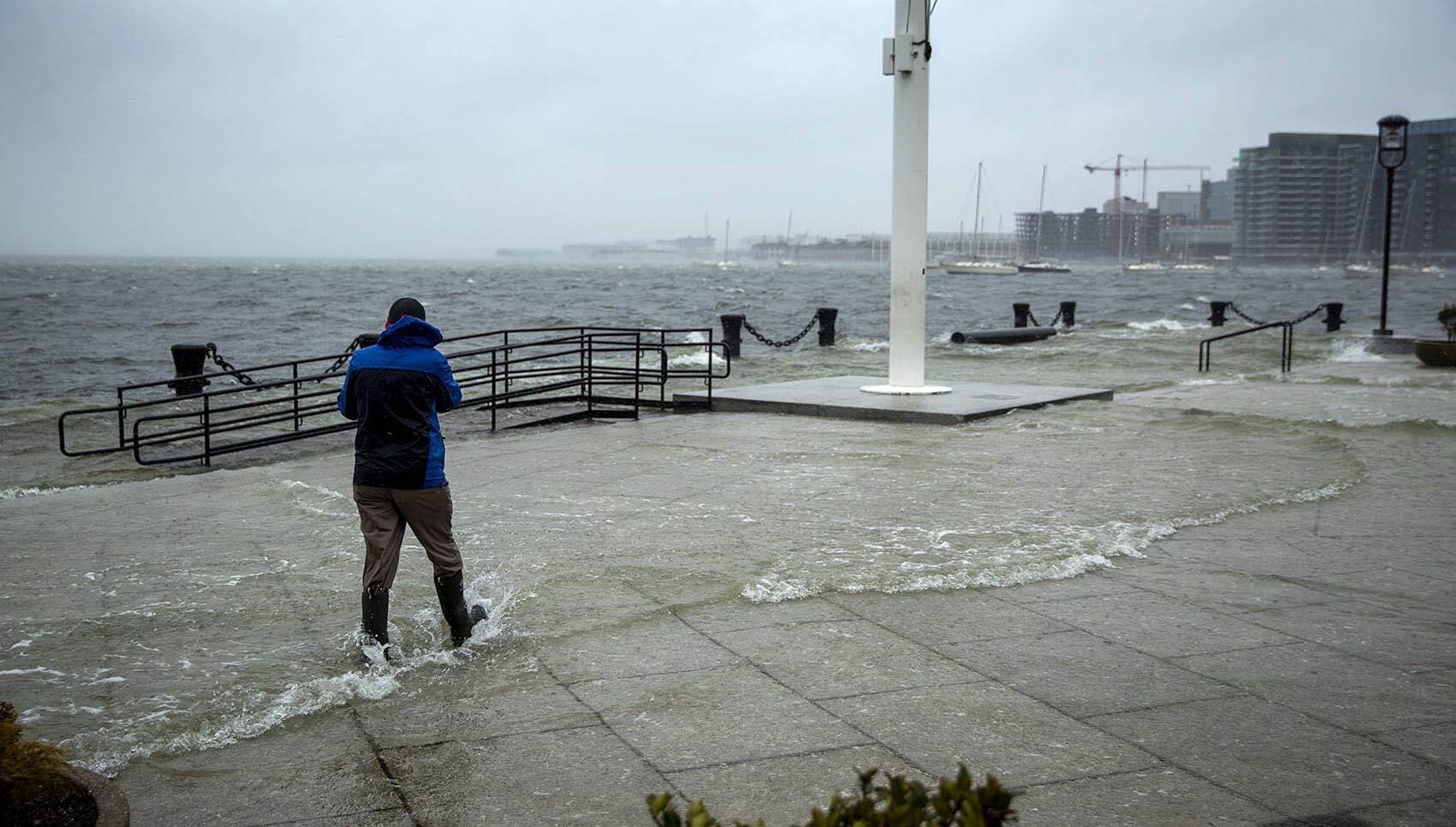 A man walks through water flooding over Long Wharf in Boston. (Robin Lubbock/WBUR)