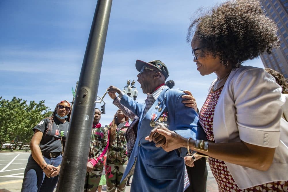 Boston Mayor Kim Janey holds the hand of Tuskegee Airman Enoch “Woody” Woodhouse as he turns the lever to raise the Juneteenth Flag at a ceremony at City Hall on Friday. (Jesse Costa/WBUR)