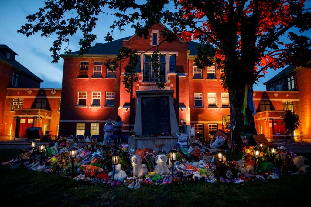 A makeshift memorial to honor the 215 children whose remains have been discovered buried near the facility is seen as orange light drapes the facade of the former Kamloops Indian Residential School in Kamloops, British Columbia, Canada, on June 2, 2021. (Cole Burston/AFP/Getty Images)