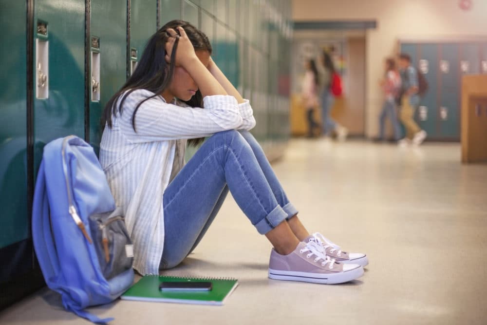 A frustrated teenager sits against the lockers in a school hallway. (Getty Images)