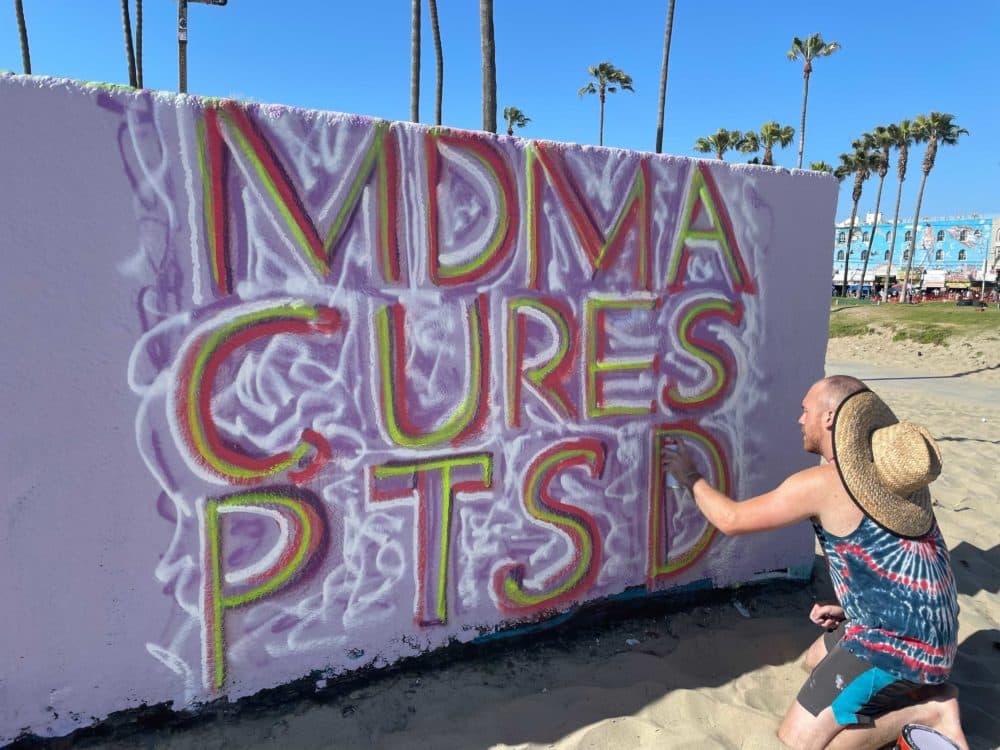 Andrew Patalano spray paints &quot;MDMA cures PTSD&quot; on May 22, 2021, in Venice Beach, California. (Tonya Mosley/Here & Now)