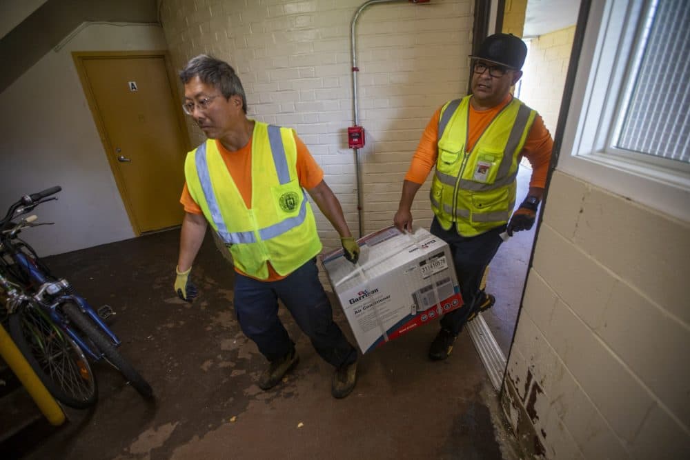 Chelsea Public Works staff Wai Leong and Cesar Cortez deliver a window air conditioner unit to a resident at the Prattville Apartments public development in Chelsea. (Jesse Costa/WBUR)
