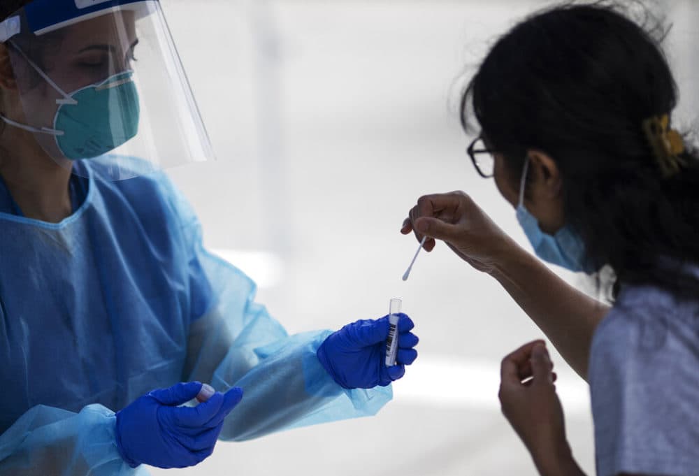 A woman is instructed on how to swab her nose by a medical worker at a free COVID-19 testing site in July 2020 in Chelsea. (David Goldman/AP)