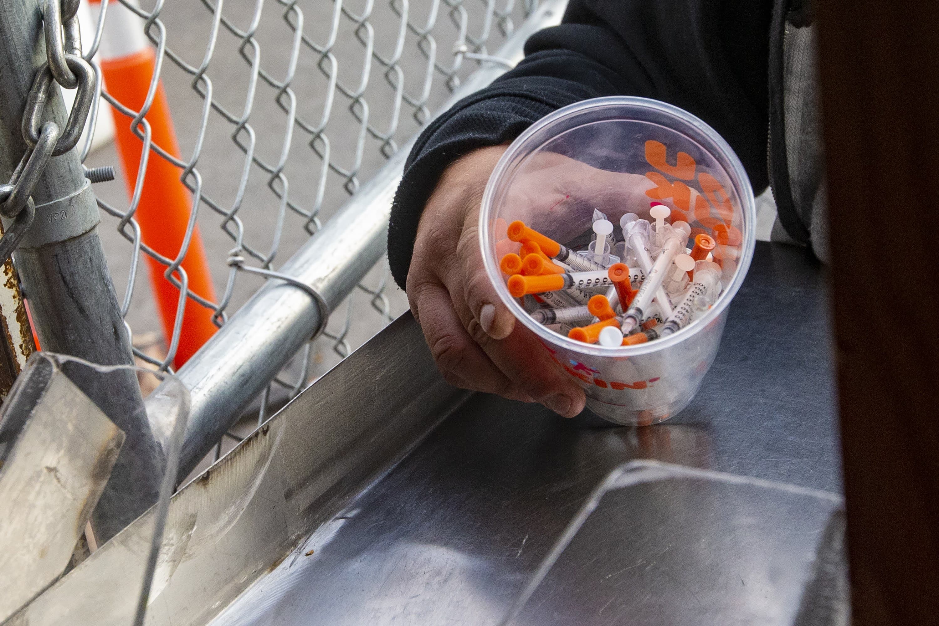 A man prepares to dump out a cup full of syringes at onto the counter as part of a syringe buy-back project in Boston run by the Community Syringe Redemption Program. (Jesse Costa/WBUR)
