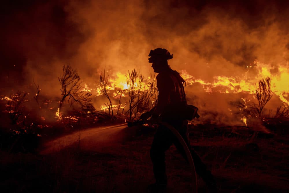 A firefighter hoses down areas of the Dixie Fire as it jumps Highway 395 south of Janesville, Calif., on Monday, Aug. 16, 2021. (Ethan Swope/AP)