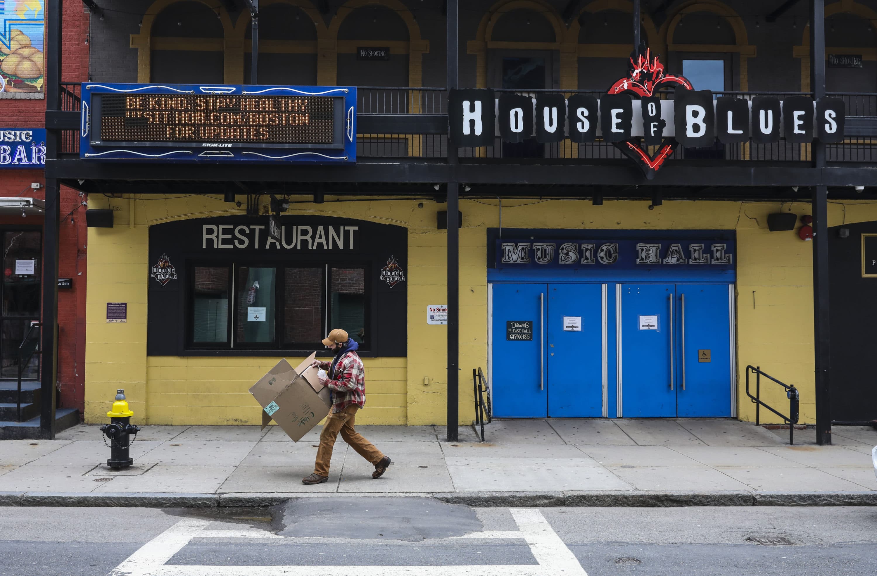 A man breaks down a cardboard box while walking past the House of Blues' COVID-19 sign urging people to be kind and stay healthy in April 2020. (Erin Clark/The Boston Globe via Getty Images)
