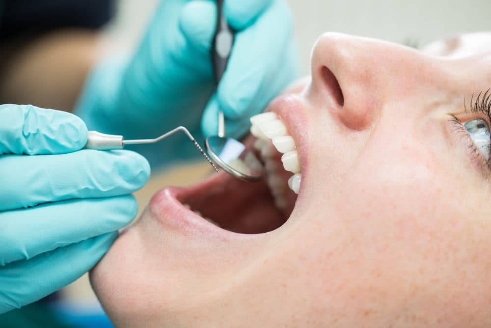 Close up of dentist holding angled mirror and hook while examining a patient. (Getty Images)