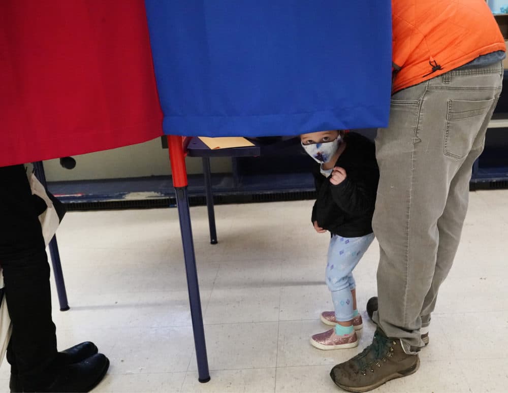 A child peeks out from the voting booth as voters mark their ballots during early in-person voting, Thursday, Oct. 29, 2020, in Cambridge, Mass. (Elise Amendola/AP)
