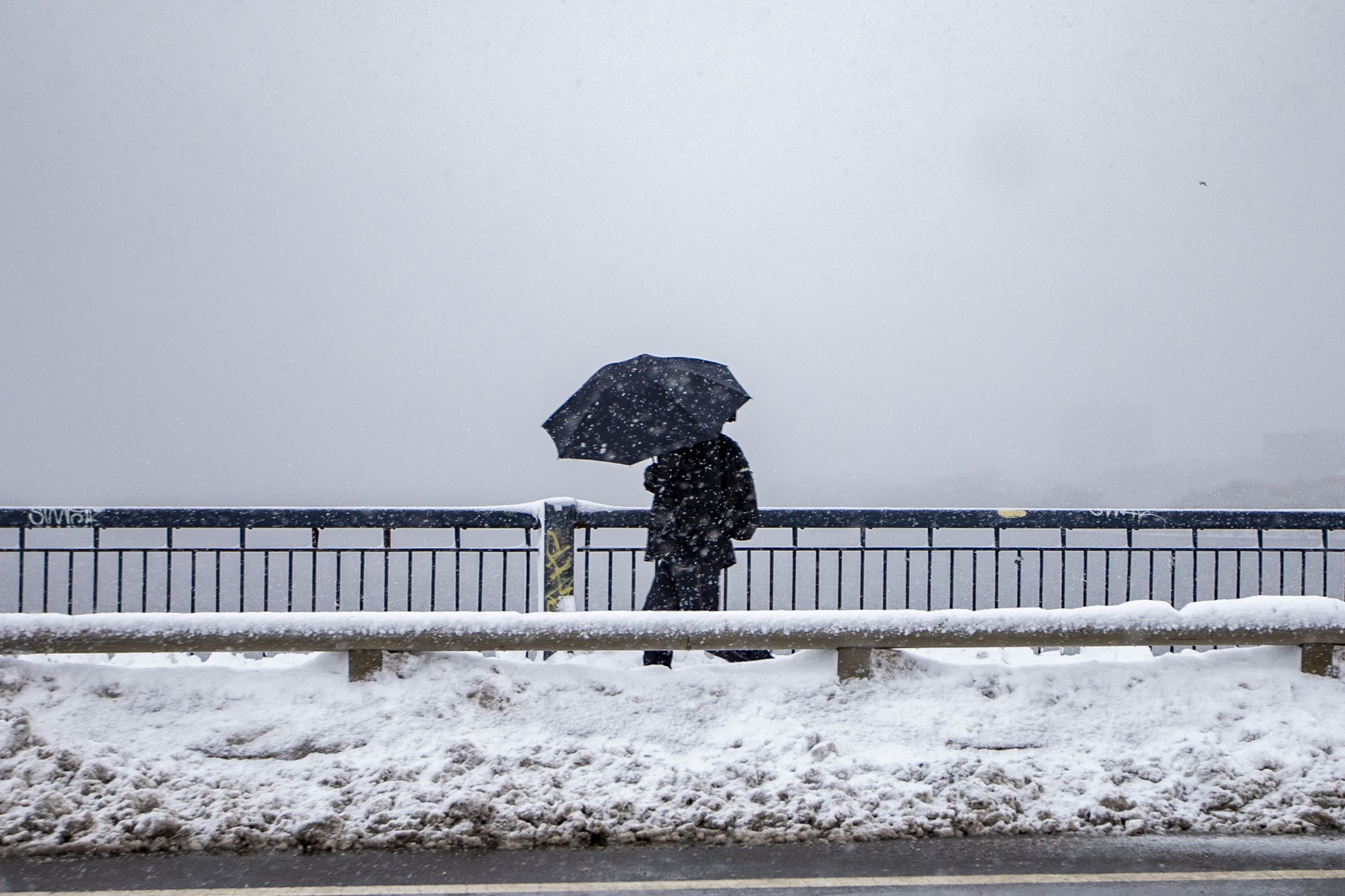 A man with an umbrella walks across the Massachusetts Avenue Bridge early Friday morning during the snowstorm. (Jesse Costa/WBUR)