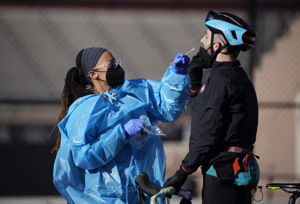 A medical technician performs a nasal swab test on a cyclist queued up in a line with motorists at a COVID-19 testing site near All City Stadium Thursday, Dec. 30, 2021, in southeast Denver. (David Zalubowski/AP)