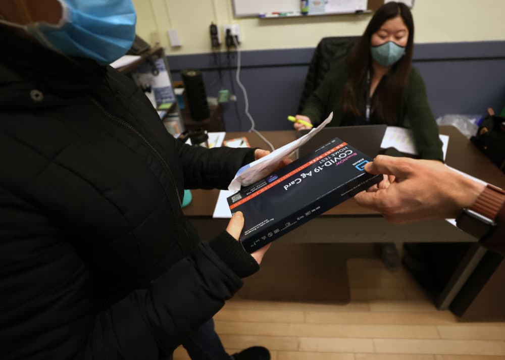 A teacher gets a COVID-19 test kit handed to her by Jordan Weymer, the school principals at the Donald McKay K-8 school in East Boston, on Jan. 3, 2022, the day before kids return back from winter break. (David L. Ryan/The Boston Globe via Getty Images)