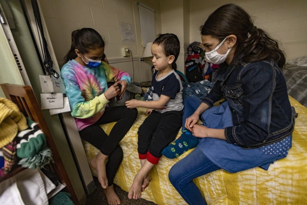 Malija, 12, Sanjar, 5, and Hadya, 10, play with a smartphone in their living quarters in the basement of St. Paul's Episcopal Church in Newburyport. (Jesse Costa/WBUR)