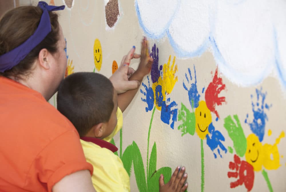 A preschool teacher helps a little boy paint flowers on a colorful exterior mural using his handprint. (Getty Images)