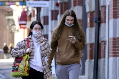 A passer-by adjusts her mask, left, while walking on a sidewalk on Newbury Street in Boston. (Steven Senne/AP)