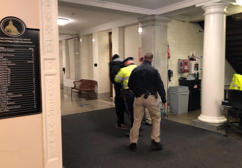 Troopers lead a man through the Ashburton Park entrance and down a State House corridor Tuesday afternoon. The State Police said two people were arrested after trying to rush past the security checkpoint. (Colin A. Young/SHNS)
