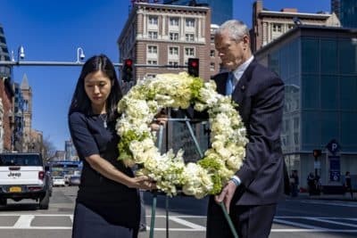Mayor Michelle Wu and Gov. Charlie Baker carry a wreath to place it at the Marathon Bombing Memorial at 755 Boylston St., the site of the second bomb explosion, to honor those who died there. (Jesse Costa/WBUR)
