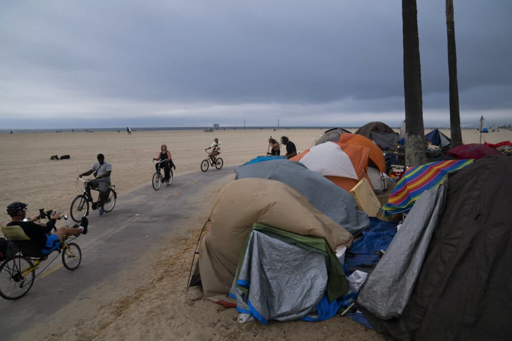 FILE - People ride their bikes past a homeless encampment set up along the boardwalk in the Venice neighborhood of Los Angeles on June 29, 2021. California's governor proposed a plan on Thursday, March 3, 2022, to force homeless people with severe mental health and addiction disorders into treatment.   (AP Photo/Jae C. Hong, File)