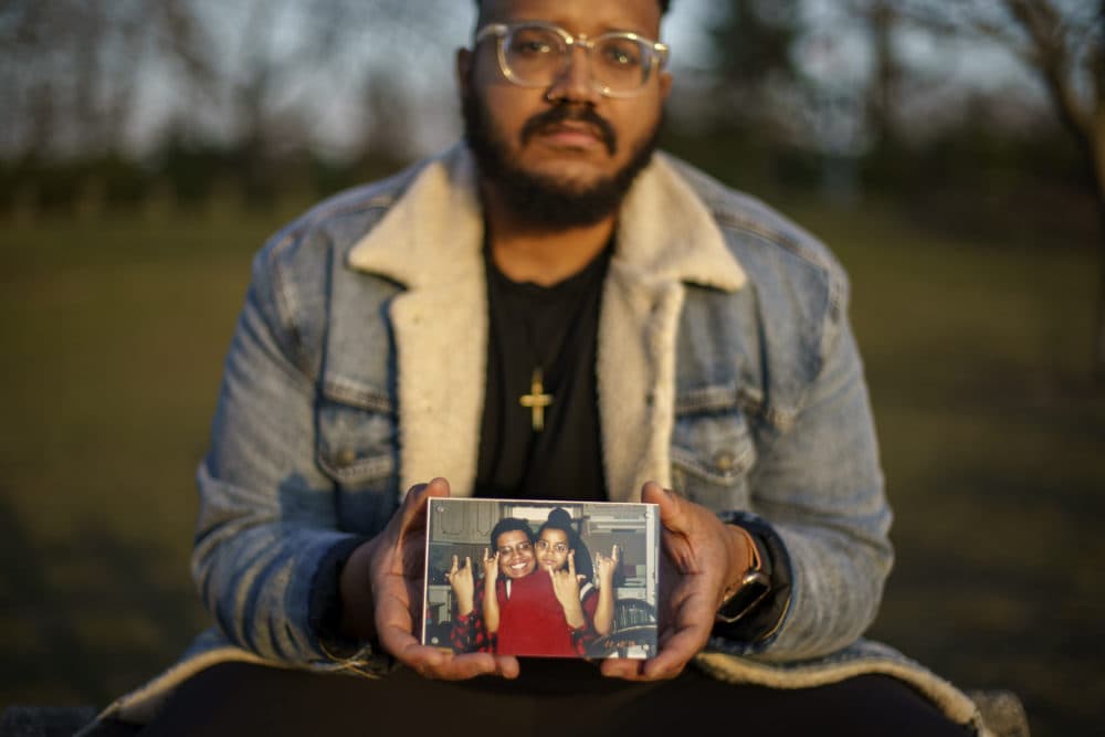 Adam Almonte holds a photo of him with his older brother, Fernando Morales, on a bench where they used to sit and eat tuna sandwiches after playing catch in Fort Tryon Park in New York, Wednesday, March 16, 2022. Morales died April 7, 2020 from COVID-19 at age 43. (AP Photo/David Goldman)