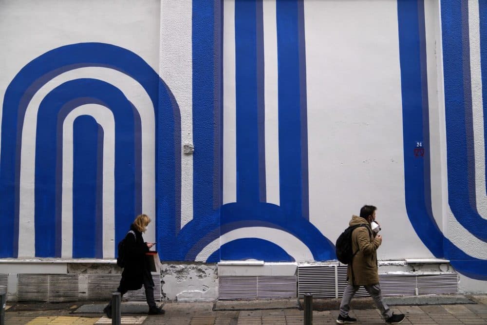 Pedestrians wearing face masks to curb the the spread of coronavirus, pass in front of the mural &quot;Waves&quot; by the artist Adioshpe in Athens, Greece, Wednesday, Jan. 12, 2022. According to health authorities Tuesday, the surge of the Omicon variant in Greece seems to have &quot;slowed down.&quot; (AP Photo/Thanassis Stavrakis)