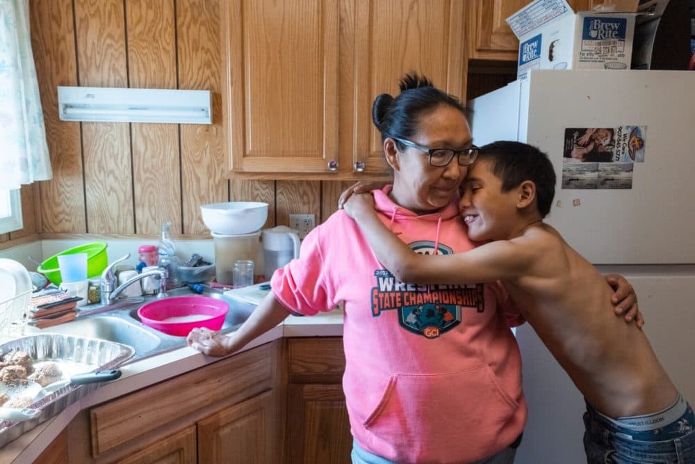 Pamela Tai and her son, Chase Tai, embrace in the kitchen while Pamela prepares dinner for firefighters. Women in the community have organized to feed up to 180 firefighting personnel who have flown into fight the East Fork Fire. June 11, 2022 in St. Mary's, Alaska. (Katie Basile/KYUK)
