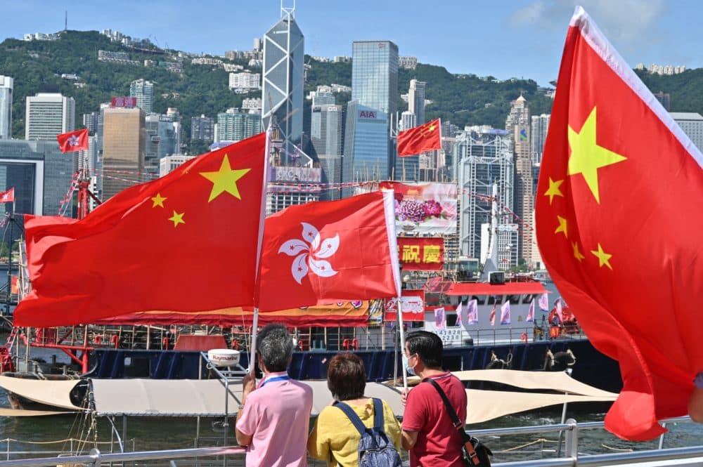 People wave Chinese and Hong Kong flags as fishing boats with banners and flags to mark the 25th anniversary of the Handover of Hong Kong from Britain to China sail through Hong Kongs Victoria harbour on June 28, 2022. (Peter Parks/AFP via Getty Images)