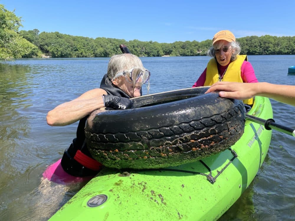 Mary Grauerholz, 72, hoists a car tire found at the bottom of Flax Pond onto a kayak. This is part of an effort to clean up pollution in freshwater environments. (Eve Zuckoff/WCAI)