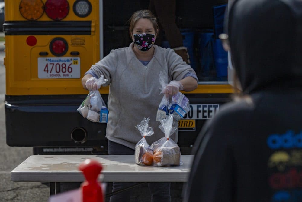 Salem public schools bus driver Sharon Moulton places bagged breakfast and lunch meals onto a table while a student waits. (Jesse Costa/WBUR)